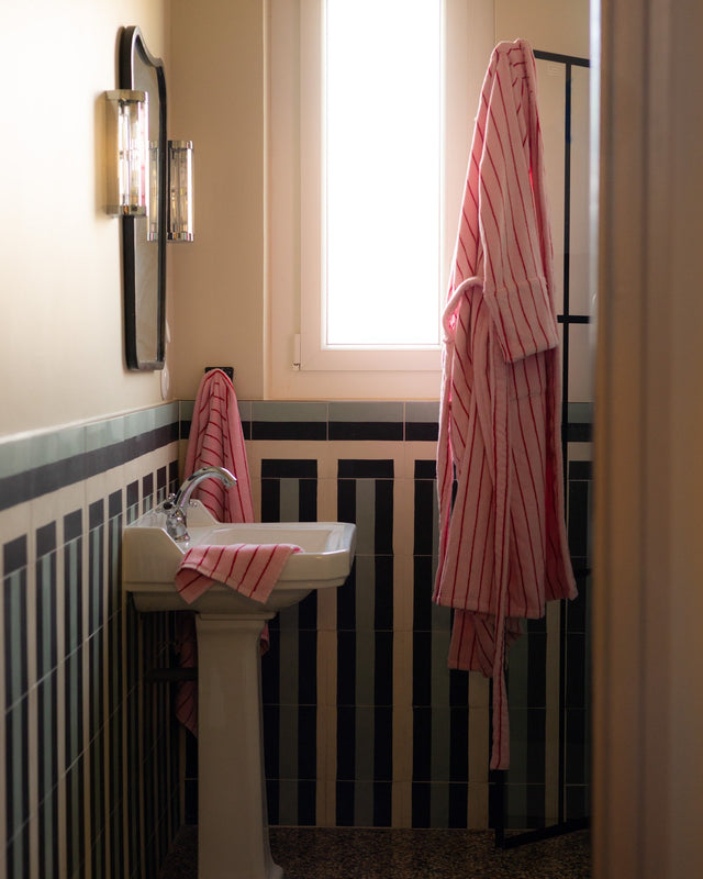 Bademantel NARAM Baby Pink & Ski Patrol Red am Haken neben einem Waschbecken mit passendem Handtuch