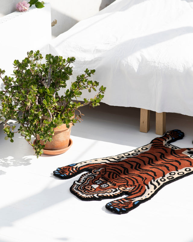 Kleiner Tiger-Teppich Frankie im Sonnenlicht vor einem Bett mit weißer Decke, daneben ein Geldbaum im Terrakottatopf
