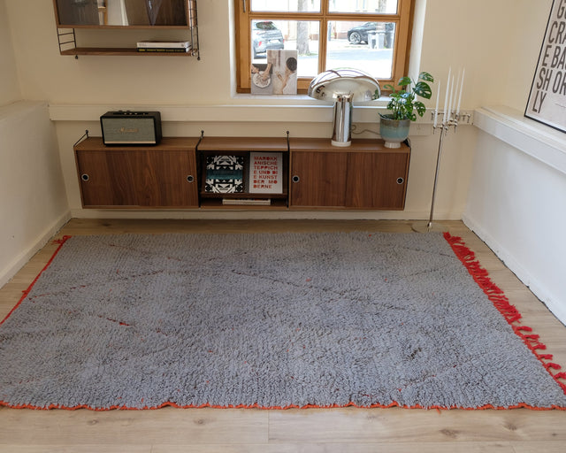 Berberteppich GREY RED 1,68 x 2,58 m im Raum: hellgrauer Flor mit roter Kante und roten Quasten