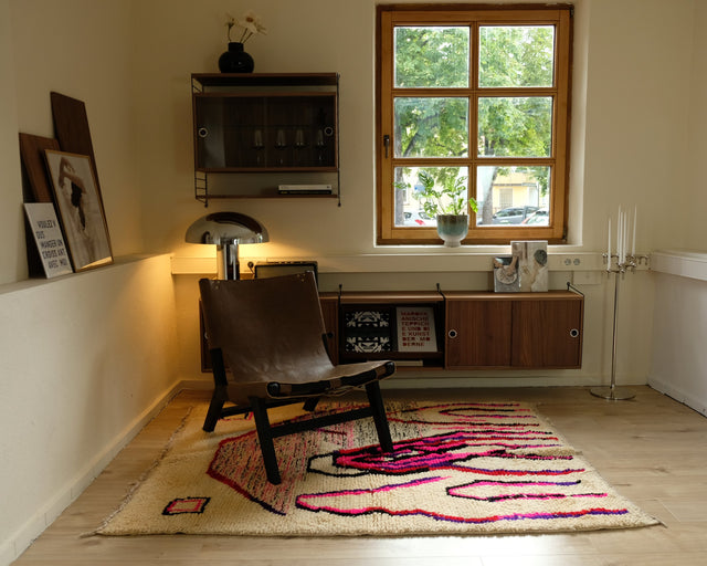 Bunter Azilal in Pink und Lila unter einem braunen Ledersessel, daneben eine leuchtende Stehlampe