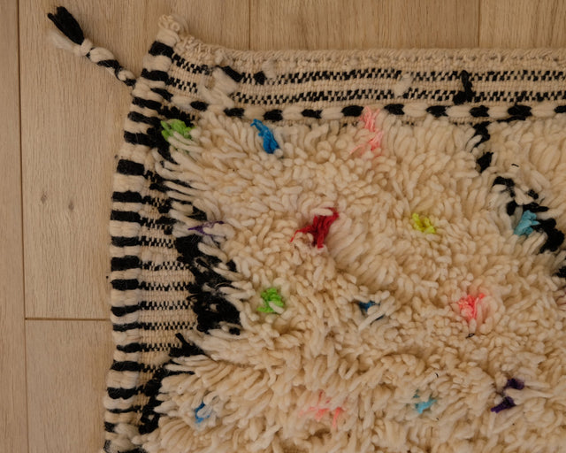 Teppichecke mit gestreiftem Kelimrand, bunten Punkten im hohen Flor und Fransen