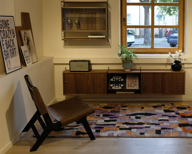 Lila Boujad im Raum mit braunem Ledersessel, dahinter ein Fenster und ein Sideboard aus Holz