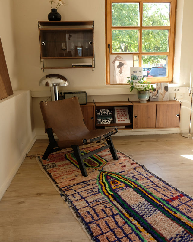 Bunter Läufer unter einem braunen Ledersessel, dahinter ein Fenster und ein Sideboard aus Holz