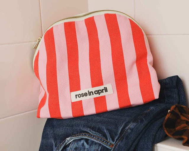 Kulturbeutel MARGAUX in Tomatenrot und Rosa auf einer Jeans im Bad, daneben ein Haargummi im Leoprint