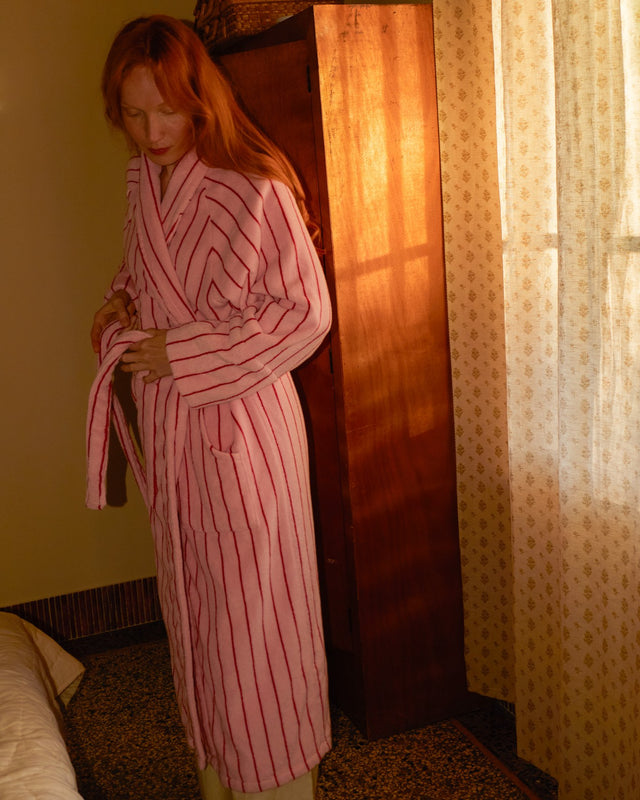 Frau mit roten Haaren bindet im Schlafzimmer den Gürtel ihres Bademantels NARAM Baby Pink & Ski Patrol Red