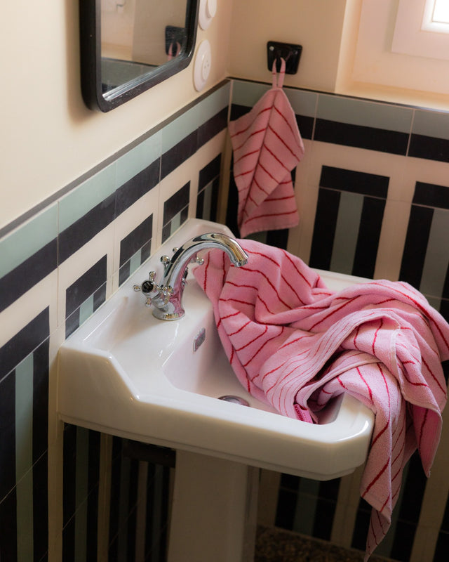 Handtuch in Baby Pink & Ski Patrol Red im Waschbecken, dahinter ein Gästehandtuch an seiner Schlaufe am Haken