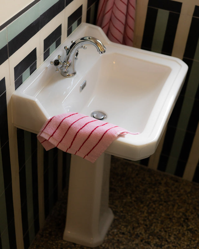 Waschlappen in Rosa mit roten Streifen auf dem Rand eines weißen Waschbeckens