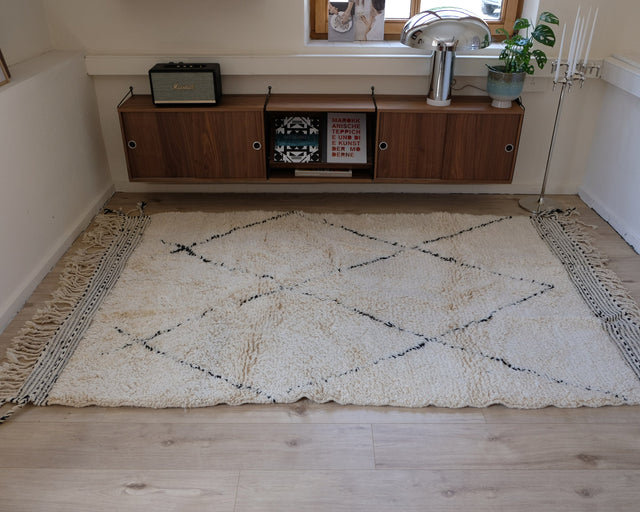 Der cremeweiße Beni Ourain liegt in ganzer Fläche vor einem Sideboard aus dunklem Holz, das Rautenmuster läuft über den ganzen Teppich.