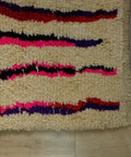 Wellige Linien in Pink, Rot, Lila und Schwarz am Teppichrand