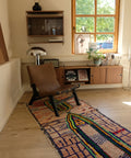 Bunter Läufer unter einem braunen Ledersessel, dahinter ein Fenster und ein Sideboard aus Holz