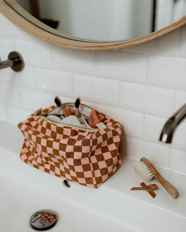 Kulturbeutel VIC Strawberry Checkerboard offen auf einem Waschtisch, darin Zahnbürsten, daneben eine Holzbürste