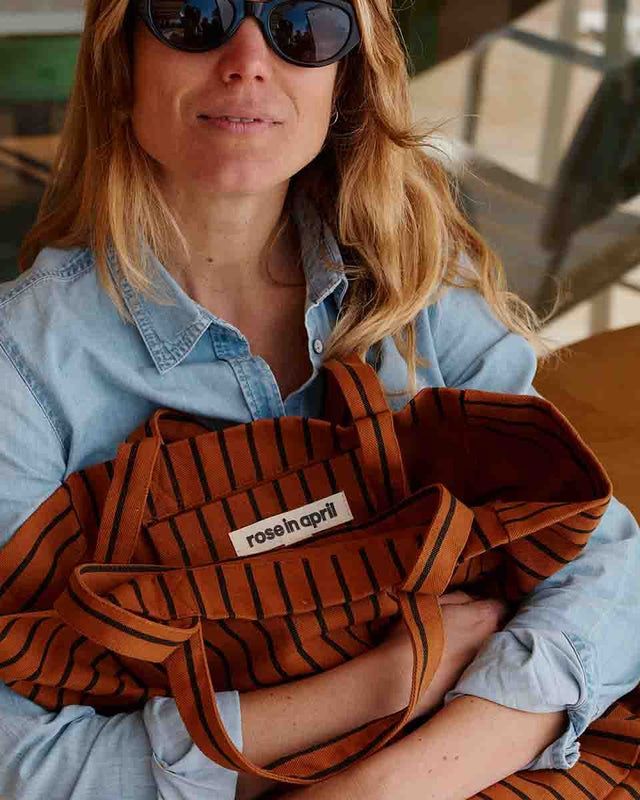 Frau im Jeanshemd mit Sonnenbrille hält die Tote Bag ELISABETH in Ginger Tennis Stripes im Arm