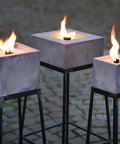 Nahaufnahme: Alle drei eckigen Betonfeuer auf Ständern  mit entzündeter Flamme.